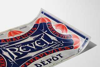 Affisch Paraplyer Revel — Registrerat varumärke, Lyon, Paris, uppsatt på ett böjt papper, sedd i perspektiv.