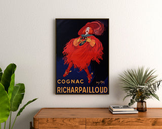 Vintageaffisch Cognac Richarpailloud, inramad ovanför en träbyrå, mellan växter.