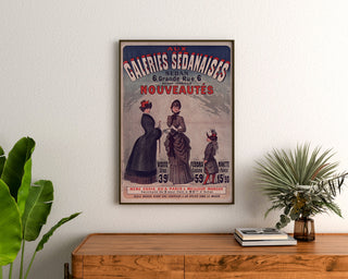 Vintage reklamaffisch Galeries sedanaises, Nouveautés, inramad ovanför en byrå i trä, mellan växter.