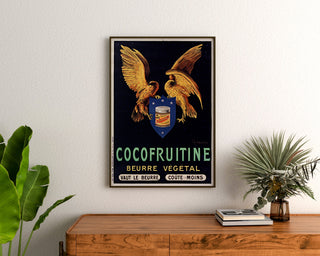 Vintageaffisch Cocofruitine, vegetabiliskt smör, inramad ovanför en träbyrå mellan gröna växter.