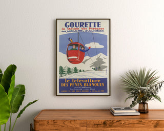 Vintageaffisch Gourette, télévoiture, inramad ovanför en träbyrå mellan krukväxter.