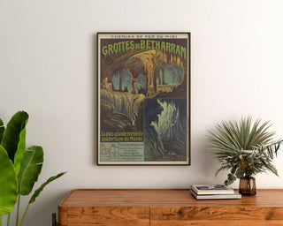 Vintageaffisch Grottes de Bétharram, inramad ovanför en träbyrå mellan krukväxter.