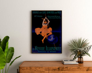 Vintageaffisch La Revue illustrée, inramad ovanför en träbyrå mellan krukväxter.