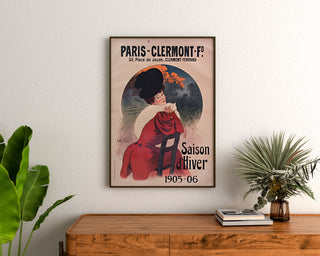 Vintageaffisch Paris-Clermont, vintersäsong, inramad ovanför en byrå i trä, mellan växter.