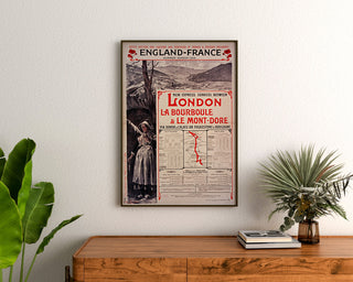 Vintageaffisch South Eastern, England-France, inramad ovanför en byrå i trä, mellan växter.
